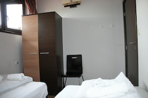 Quarto de hotel com duas camas, um guarda-roupa, uma cadeira e uma janela.