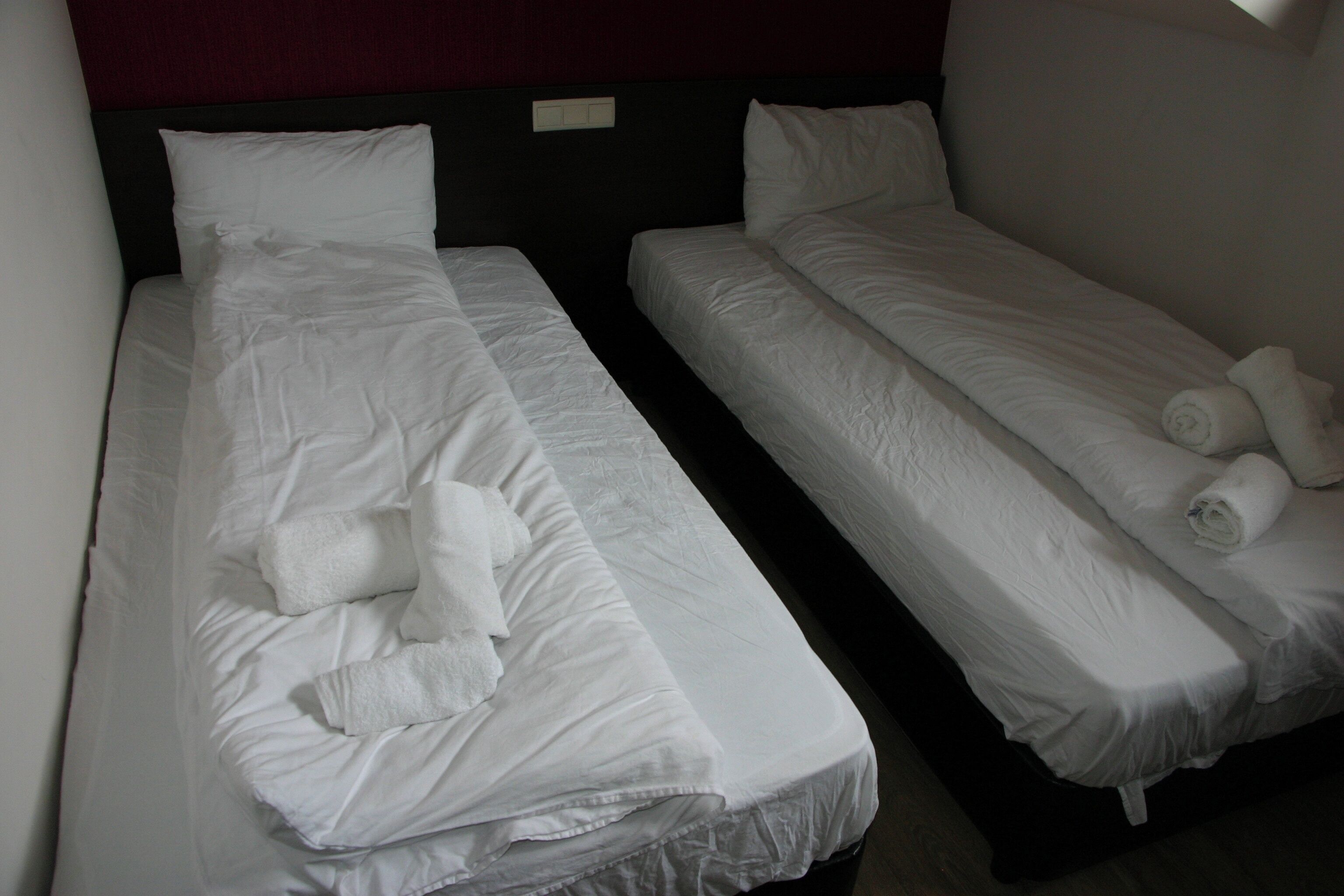 Two single beds with white linens and towels, a dark headboard, and a plain wall.