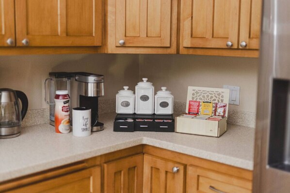 Una cocina con armarios de madera, una cafetera, una jarra de leche y frascos de especias.