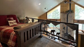 Un dormitorio acogedor con techo inclinado, cama de madera, almohada roja, ventilador de techo y vista a una chimenea de piedra.