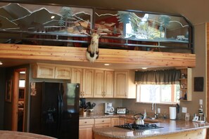 A kitchen with wooden cabinets, a black refrigerator, a stove, and a window with a view of trees.