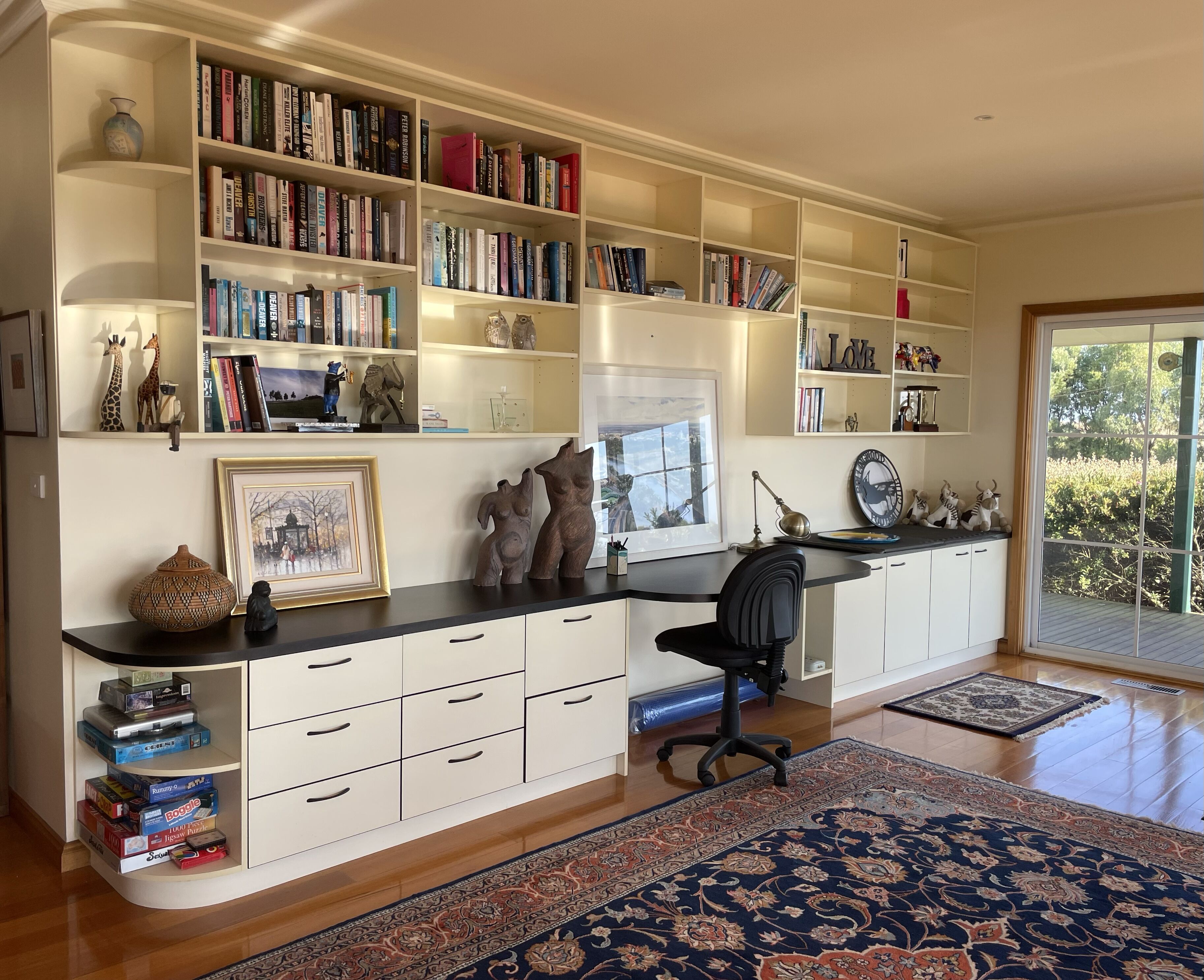 Une pièce spacieuse avec une grande bibliothèque, un bureau avec une chaise et une grande fenêtre donnant sur un paysage verdoyant.