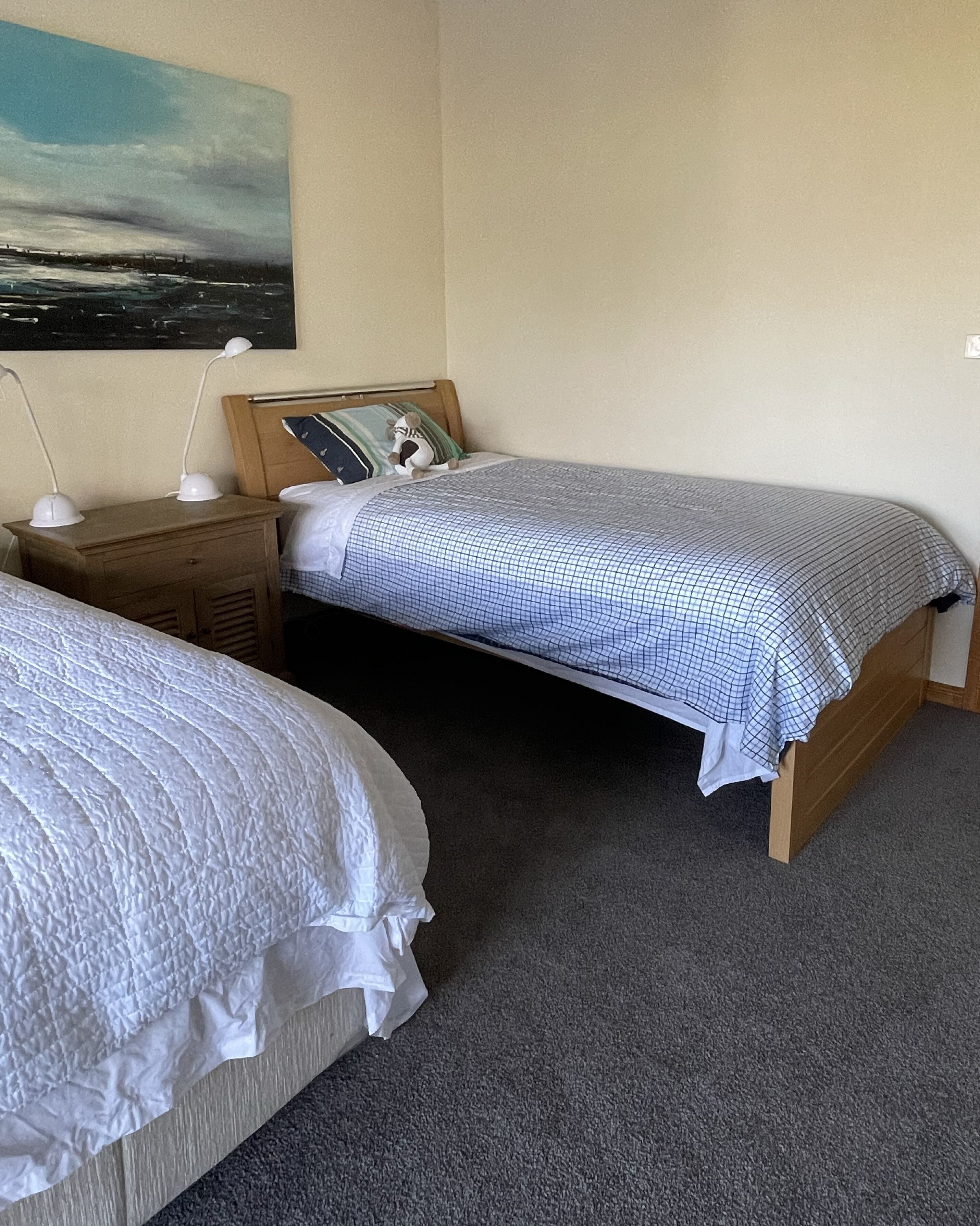 Une chambre avec deux lits simples, une table de chevet avec une lampe, une tête de lit en bois et un tableau au mur.