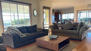 Amplia sala de estar con dos sofás, una mesa de centro y ventanas grandes con vistas al exterior.