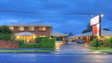 A Rosebud Gardens Motel with a brick facade, covered parking, and a well-lit entrance.