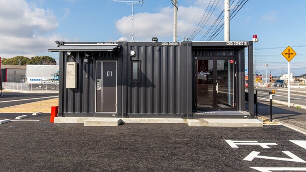 A small, modern building with a metal exterior, a door labeled "01", and a sign indicating a crossroad ahead. - HOTEL R9 The Yard Nakatsu (Nakatsu)