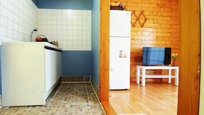 Una cocina compacta con un refrigerador blanco, una mesita con televisión y un panel de madera.