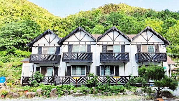 Un edificio de estilo japonés tradicional con varios balcones, rodeado de abundante vegetación y un telón de fondo montañoso.