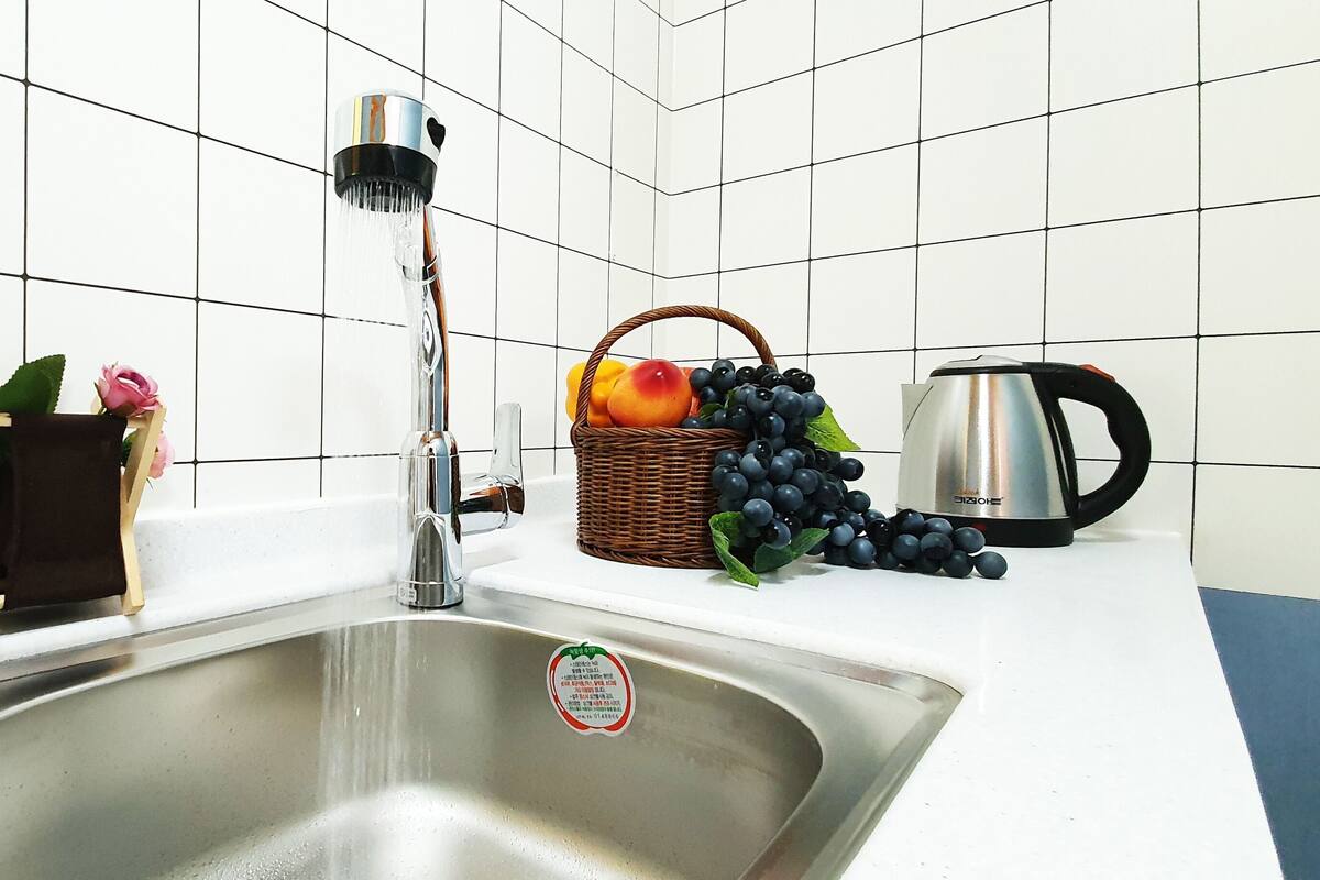Een keuken met een roestvrijstalen spoelbak, een kraan, een mand met fruit en een waterkoker.