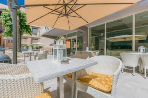 An outdoor seating area with wicker furniture and a large umbrella. - Confort (Rimini)