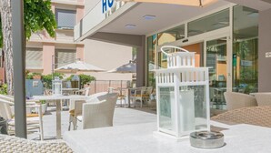 Een terras met rieten meubels, een witte tafel en een glazen overkapping.