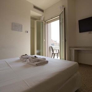 A hotel room with a bed, a flat-screen TV, a chair, and a view through an open door.