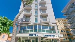 Een hotel met een moderne gevel, meerdere balkons en een heldere lucht.