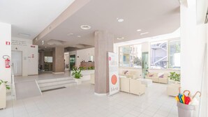 Een ruime lobby met een receptiebalie, zithoek en een groot raam met uitzicht op het omliggende gebied.