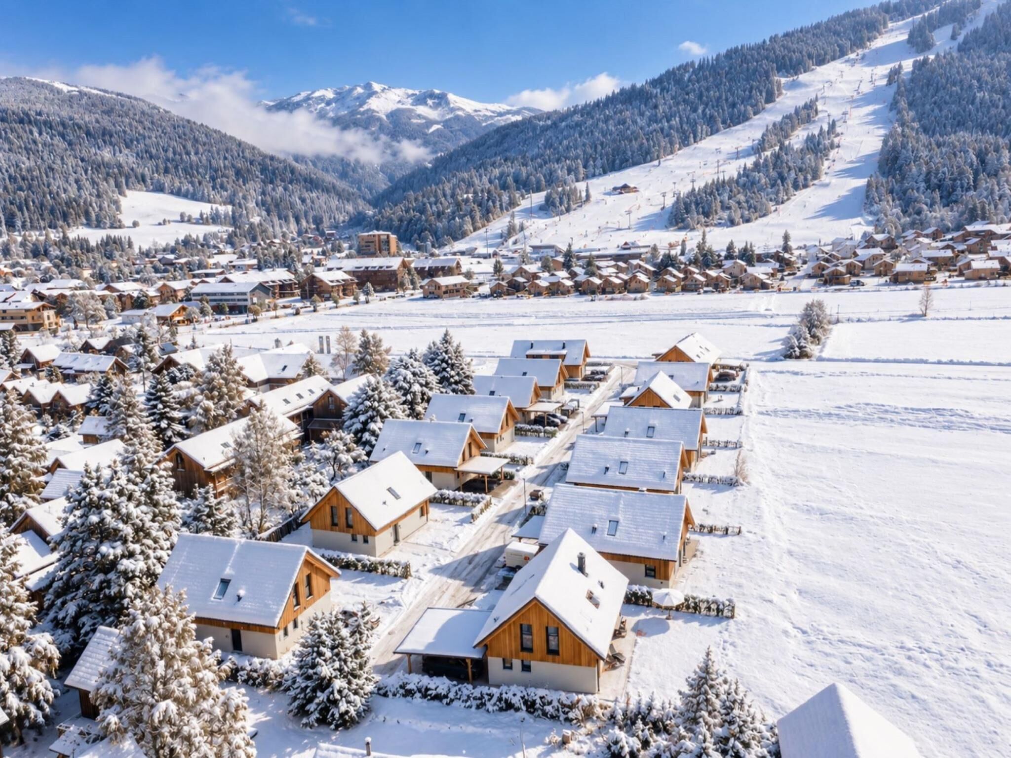 A snow-covered village with wooden houses, a ski slope, and mountains in the background.