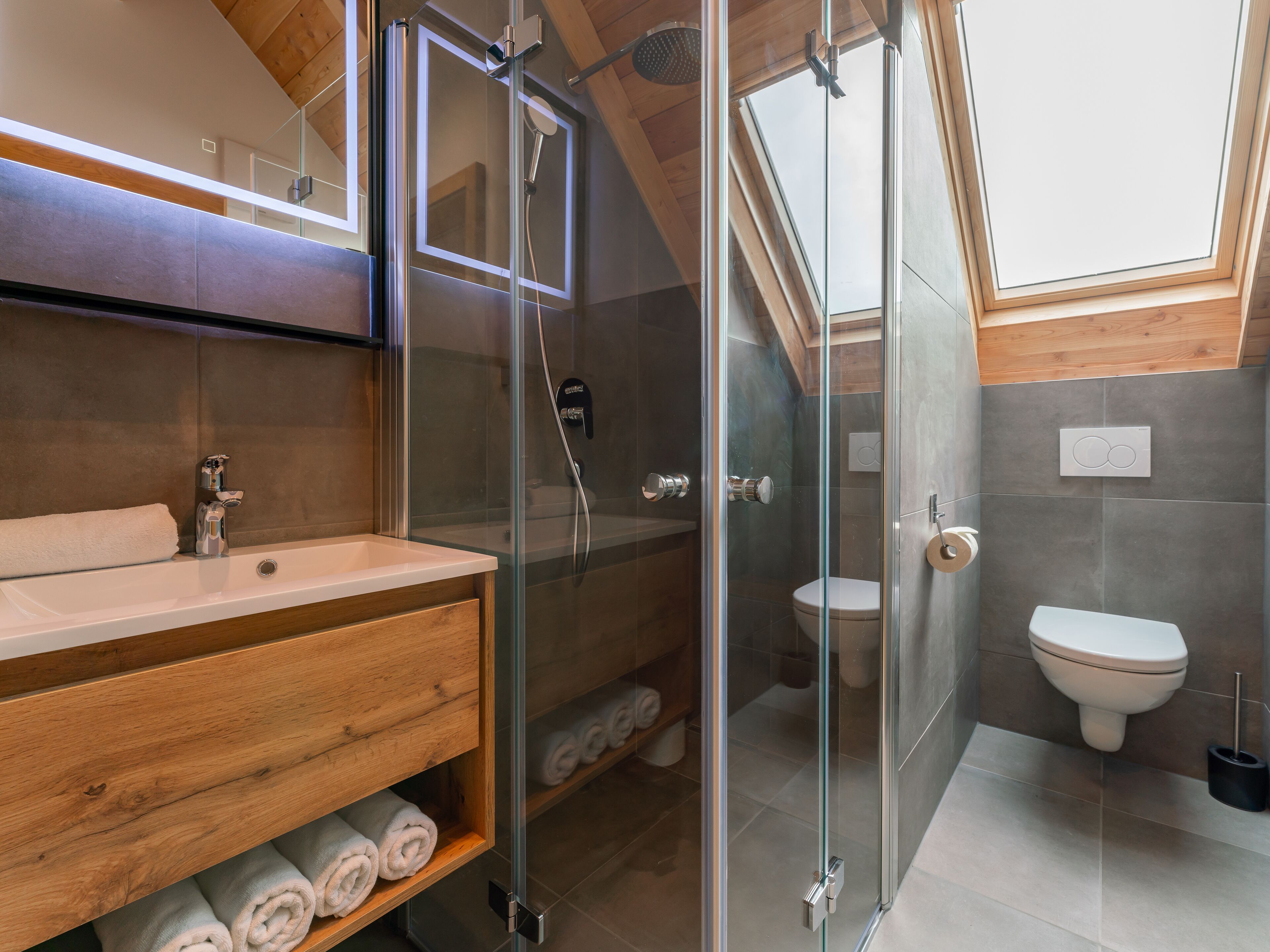 A modern bathroom with a glass-enclosed shower, a wooden vanity, and a toilet.