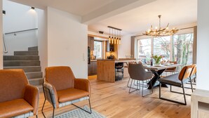 Amplia sala de estar con piso de madera, una mesa de comedor con sillas y una cocina al fondo.
