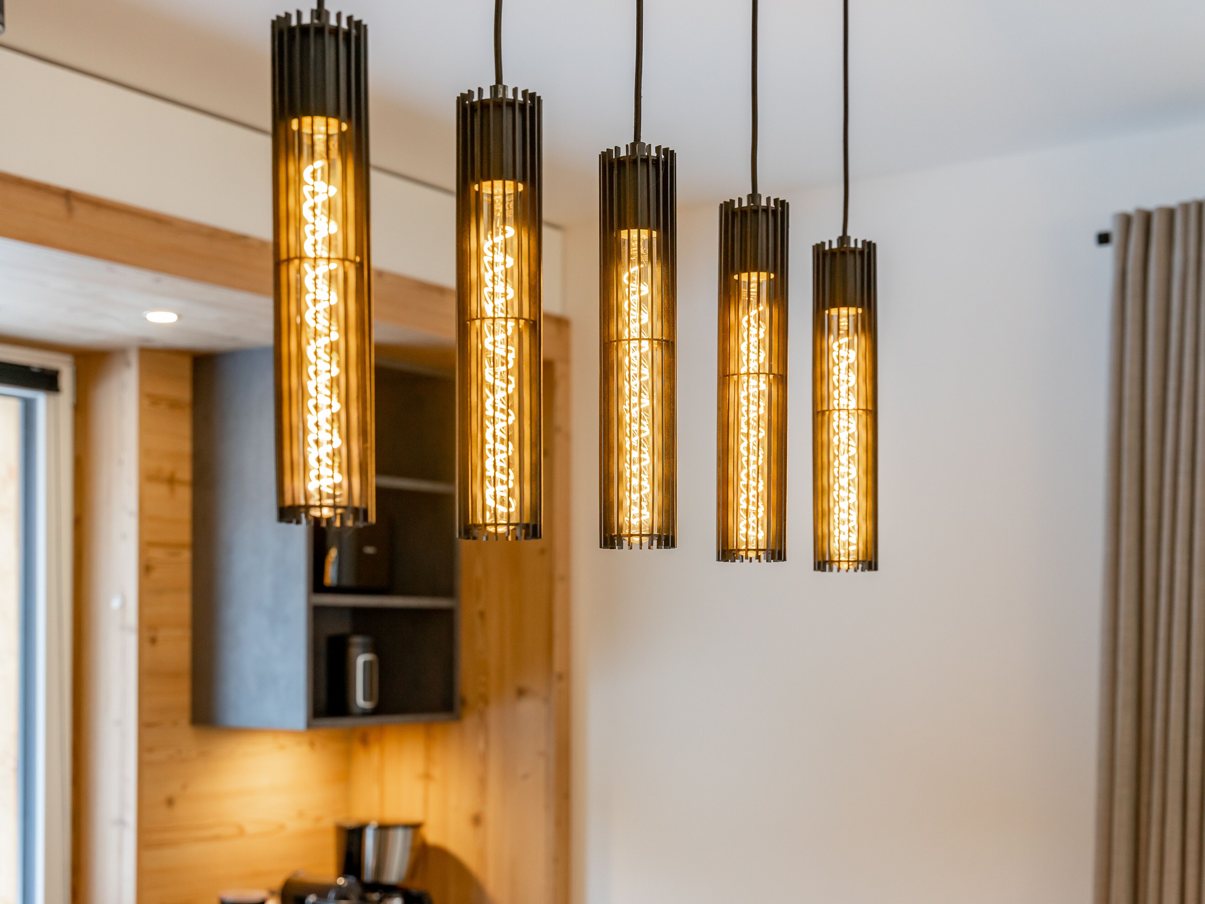 Une cuisine moderne avec des meubles en bois, une machine à café et des suspensions lumineuses aux ampoules apparentes.