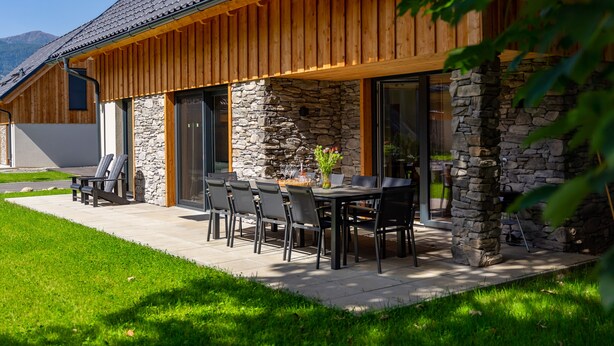 Un edificio moderno con fachada de piedra, revestimiento de madera y un patio con mobiliario exterior.