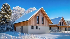 Una cabaña de madera con techo inclinado, rodeada de árboles cubiertos de nieve y un cielo azul despejado.
