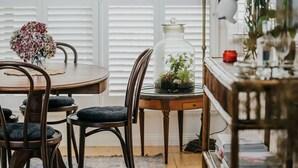 A dining area with a round wooden table, two chairs, a glass-top side table with a potted plant, and a decorative glass jar. - Candlebark Daylesford ~ Gorgeous Cottage! (Daylesford)