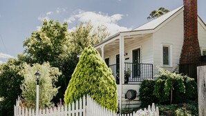 A white house with a brick chimney, a porch with a railing, and a white picket fence. - Candlebark Daylesford ~ Gorgeous Cottage! (Daylesford)