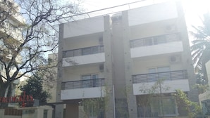 Un edificio residencial de varios pisos con balcones, entrada protegida por un portón y un coche estacionado.