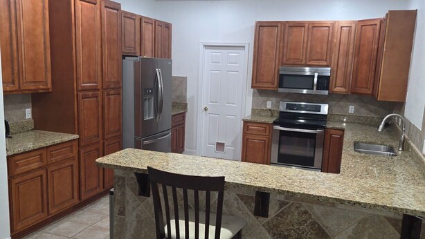 Una cocina con armarios de madera, encimeras de granito, refrigerador de acero inoxidable, microondas y estufa.