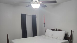 Un dormitorio con una cama, un ventilador de techo, una ventana con cortinas y una espada colgada en la pared.