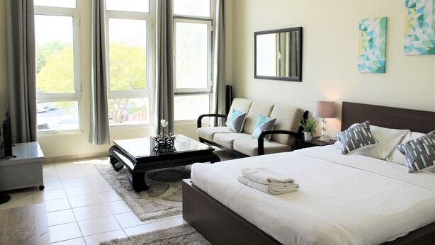 A hotel room with a bed, a sofa, a coffee table, and a TV. - IRN - Spacious Studio in Discover Garden (Dubai)