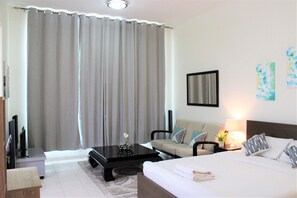 A hotel room with a bed, a sofa, a coffee table, a TV, and a lamp. - IRN - Spacious Studio in Discover Garden (Dubai)