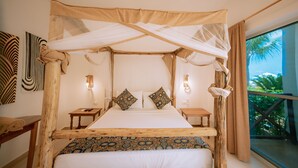 Una cama con dosel, colcha estampada, dos almohadas, mesitas de noche y vistas al verdor por una ventana.