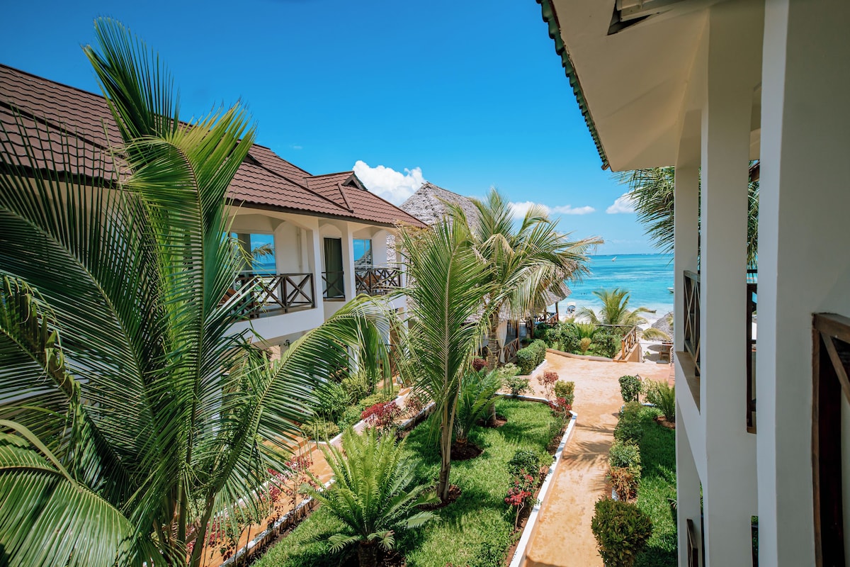 Ein Resort mit einem Weg, der zu einem Strand führt, umgeben von üppiger Vegetation und Palmen.