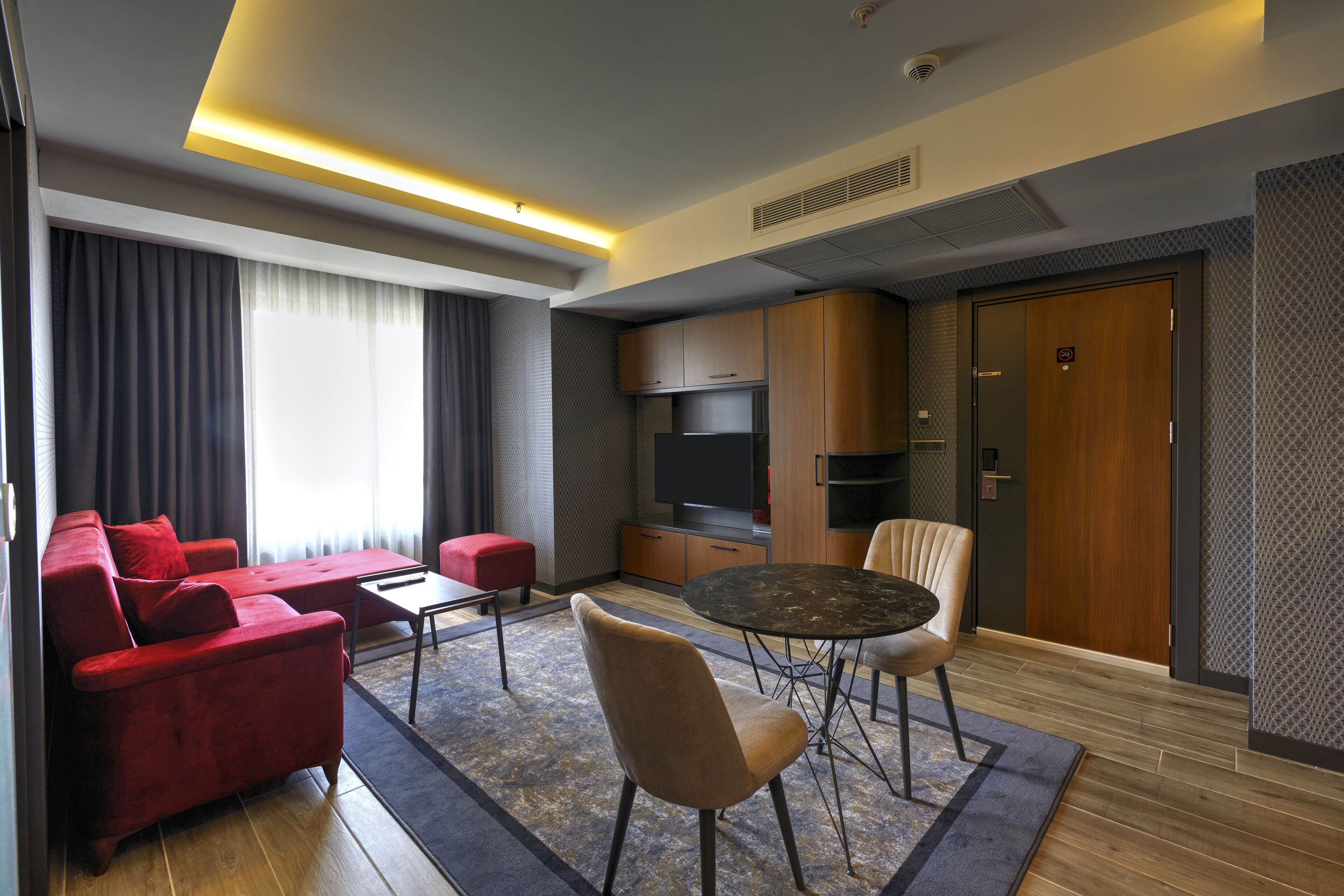 A modern hotel room with a red sofa, a round dining table, and a TV.