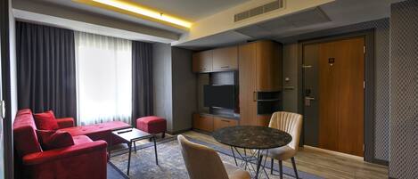 A modern hotel room with a red sofa, a round dining table, and a TV.