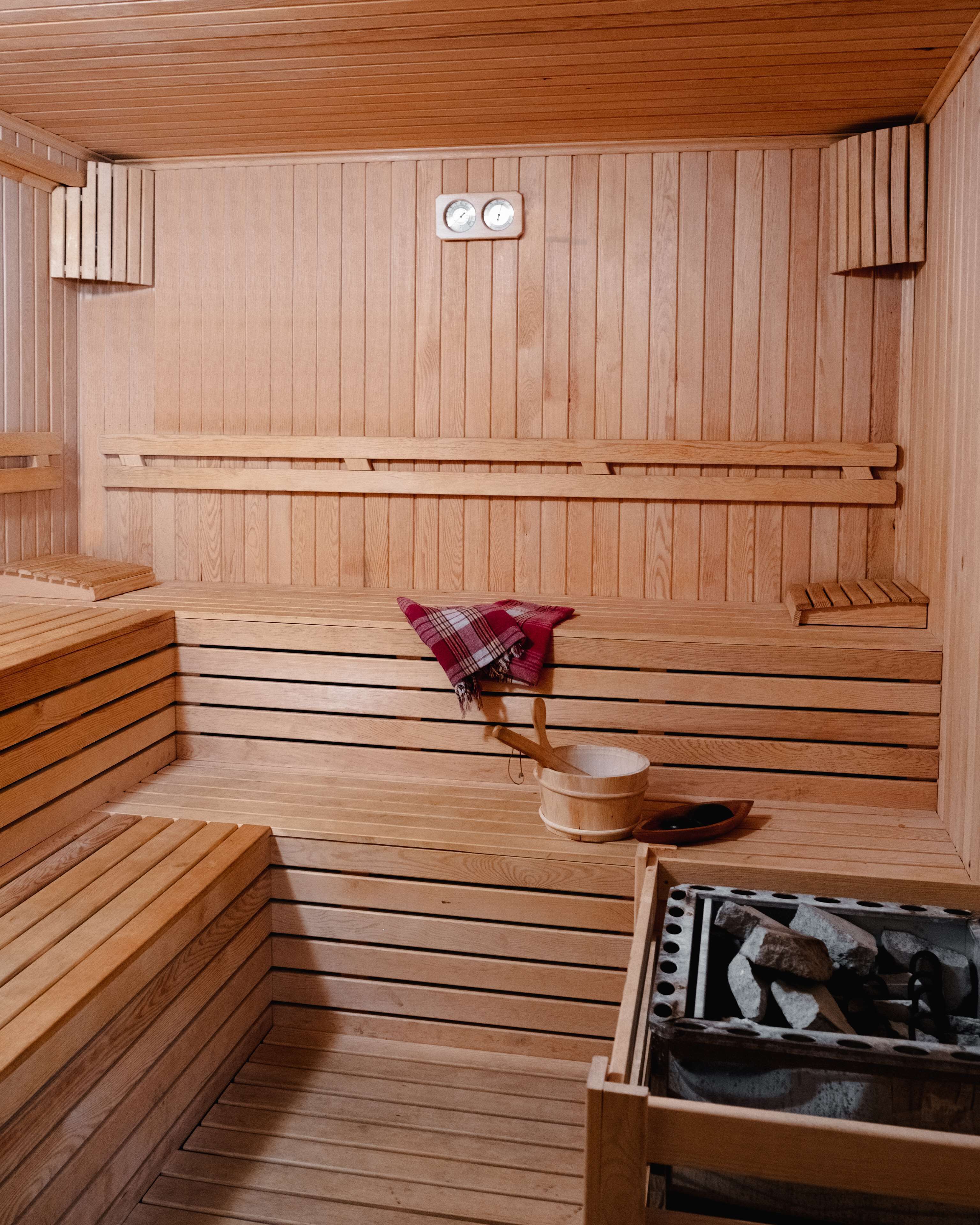 A wooden sauna with benches, a bench with a plaid towel, and a sauna heater.