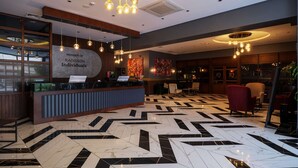 Un hall d’hôtel avec un comptoir d’accueil, des luminaires modernes et un sol à motifs.