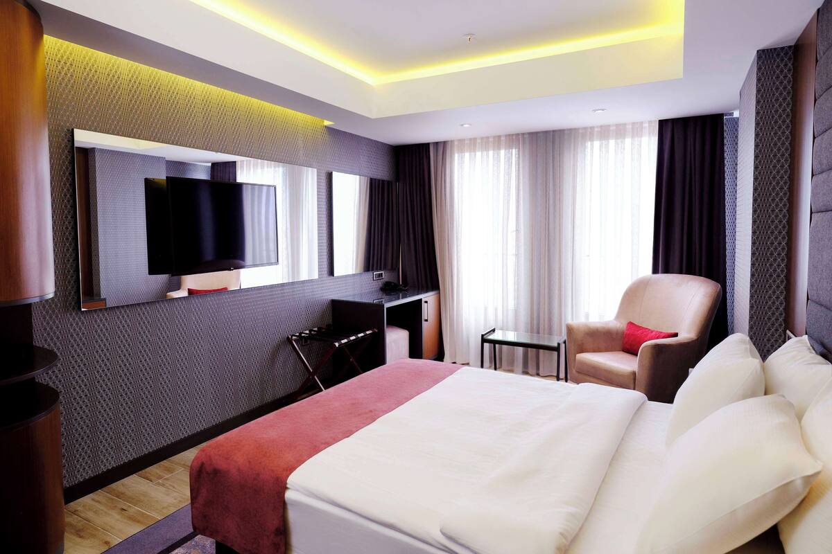 Een hotelkamer met een groot bed, een bureau, een stoel, een televisie en een raam met gordijnen.