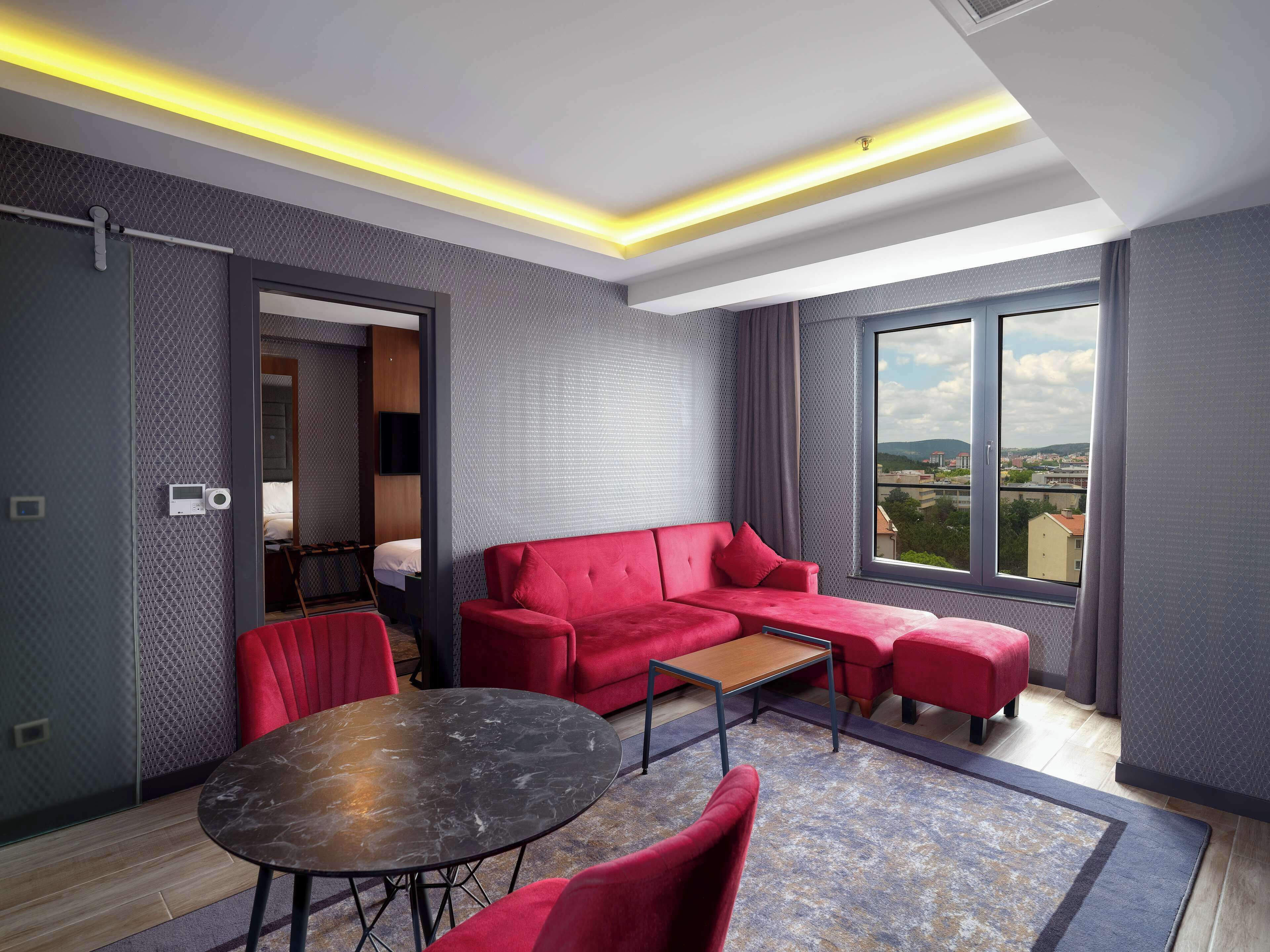A modern living room with a red sectional sofa, a round table, and a large window offering a city view.