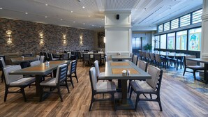 Un grand espace dédié à la salle à manger, avec plusieurs tables et chaises, un mur en briques et de grandes fenêtres.