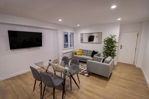 En moderne stue med et glasbord, grå sofa og et stort fladskærms-tv monteret på væggen.