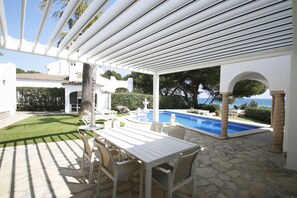 A covered patio with a pool, stone flooring, white furniture, and a view of the sea.