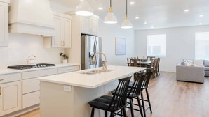 Een moderne keuken met witte kasten, een centraal eiland met barstoelen, een roestvrijstalen koelkast en hanglampen.