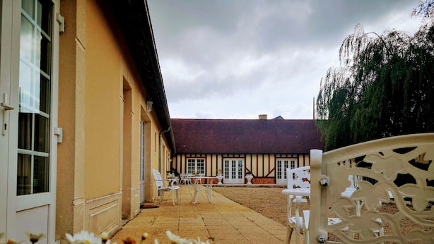 A courtyard with outdoor seating, a building with a red roof, and a garden with flowers. - Independent residence sleeps 32 (Croisilles)