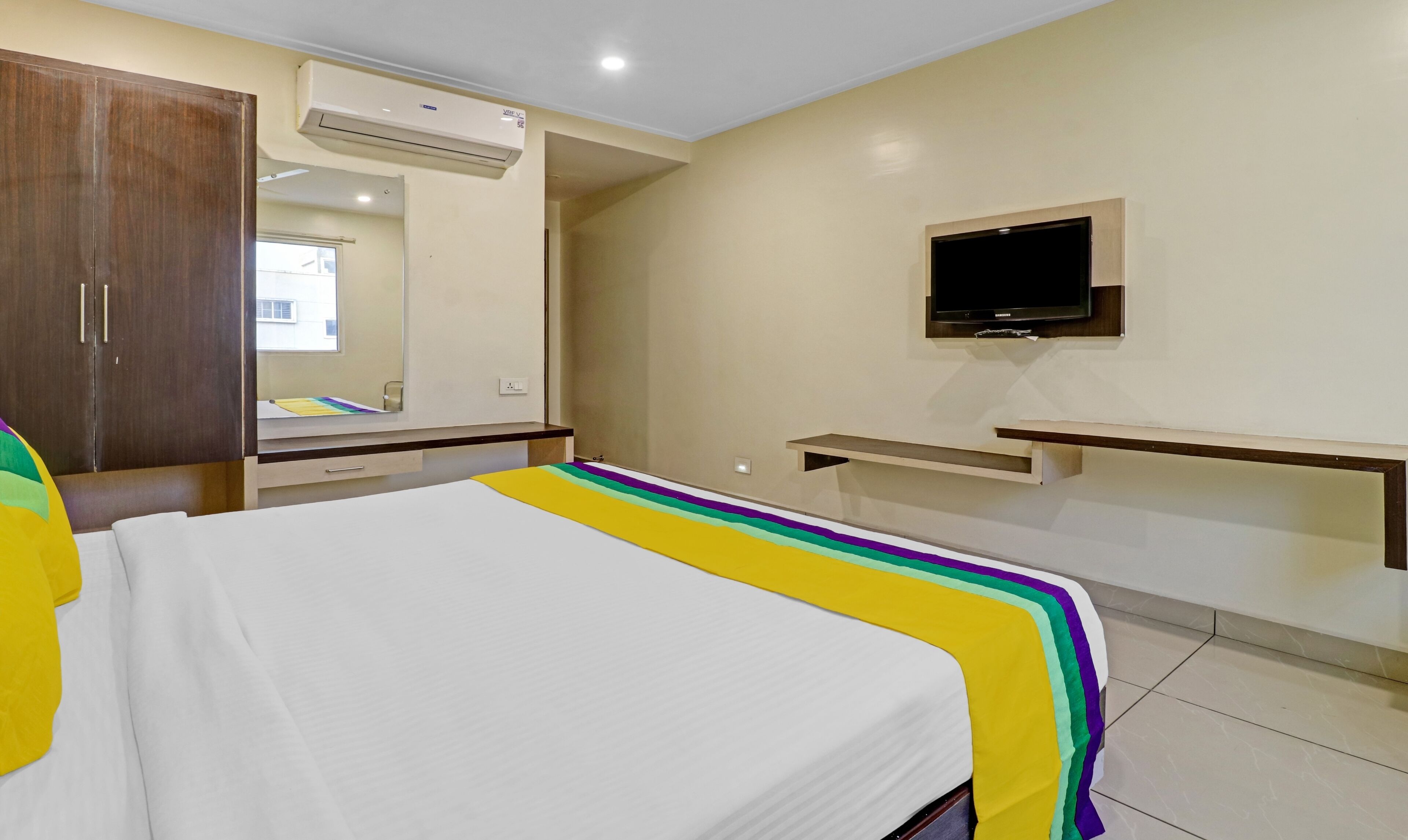 A hotel room with a bed, a wardrobe, a TV, and a mirror.