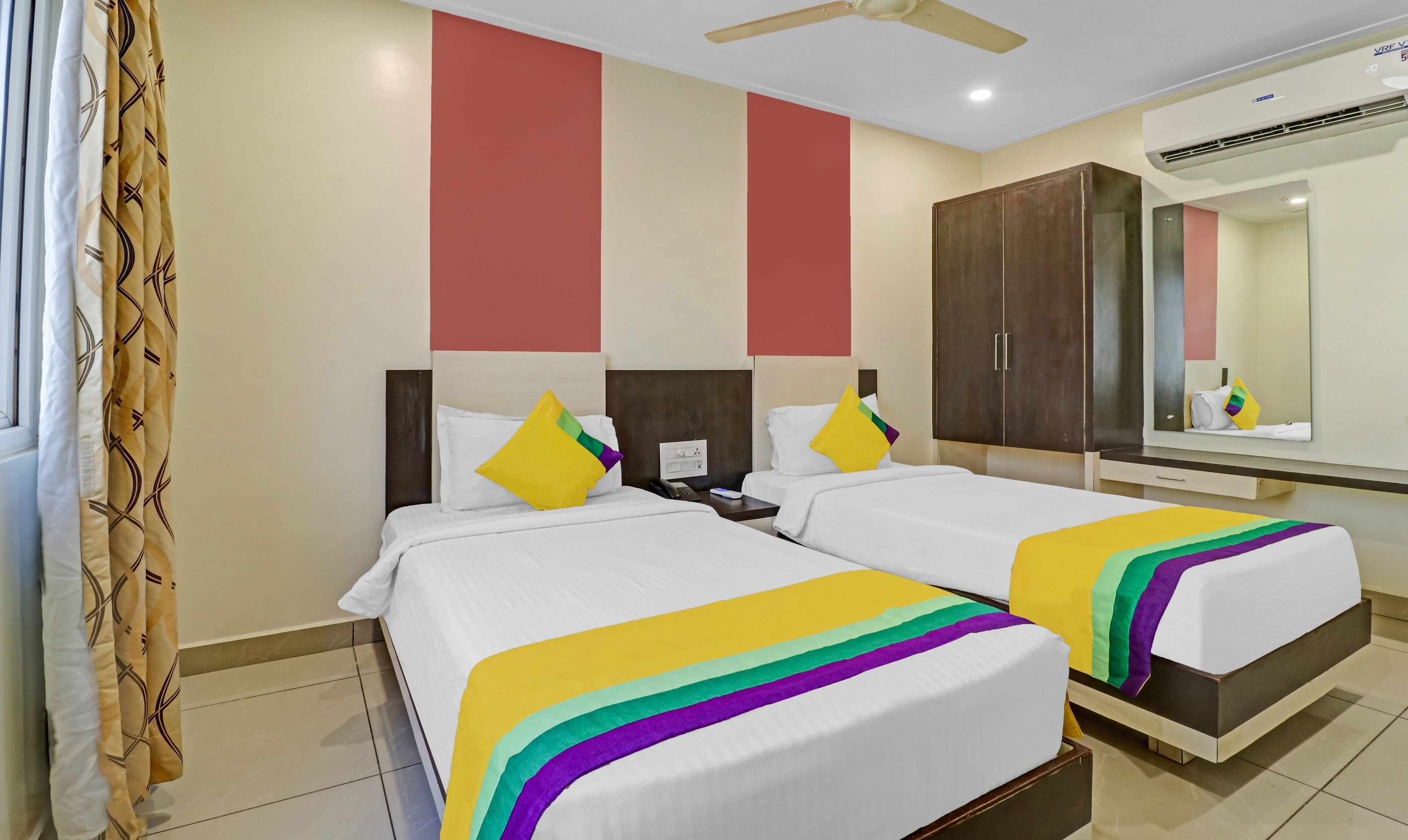 A hotel room with two beds, a large mirror, a wardrobe, and a ceiling fan.
