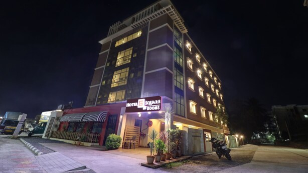 Un hôtel à plusieurs étages, avec une enseigne indiquant « Hotel Square Rooms » et une entrée bien visible.