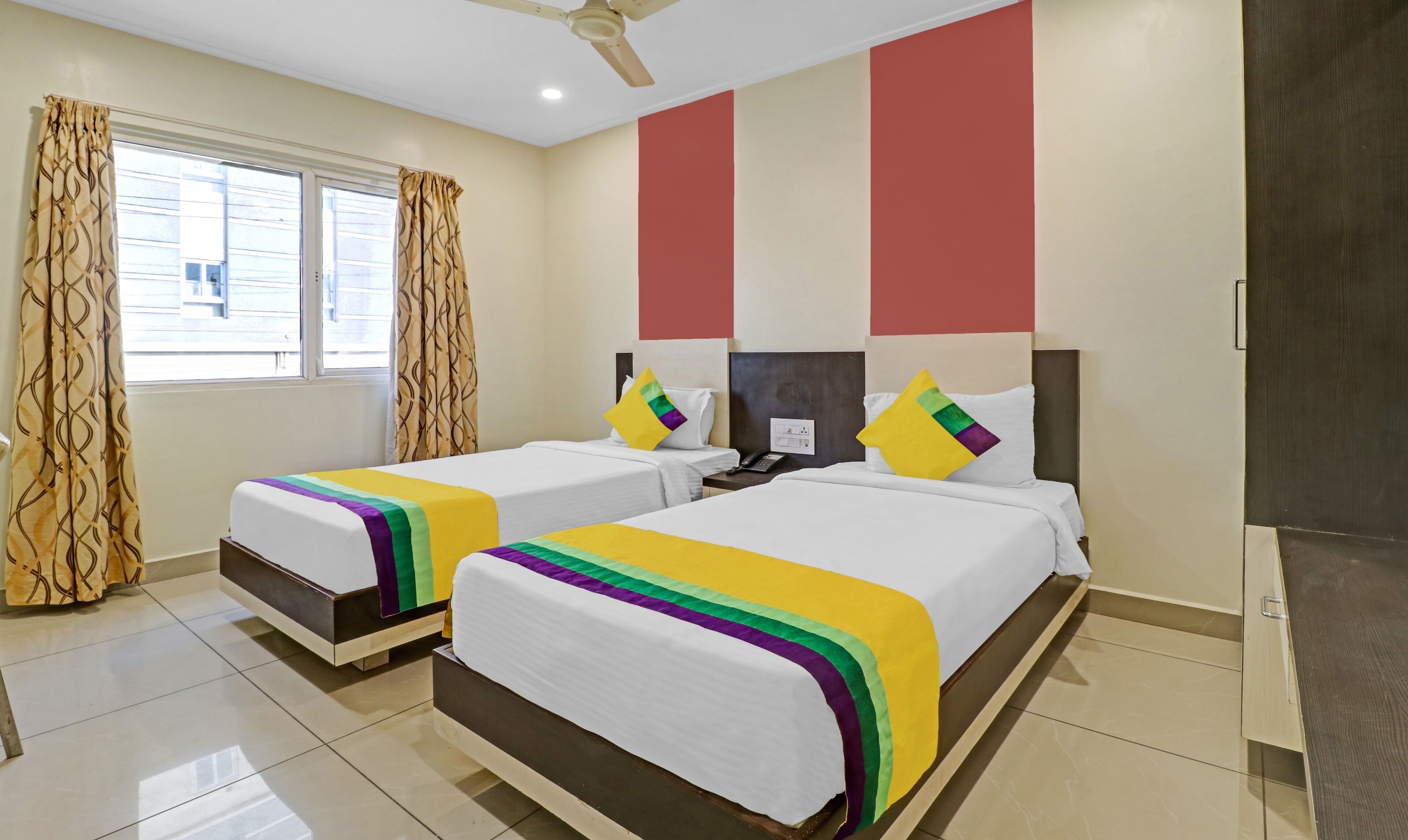 A hotel room with two beds, a window with curtains, a ceiling fan, and a door.