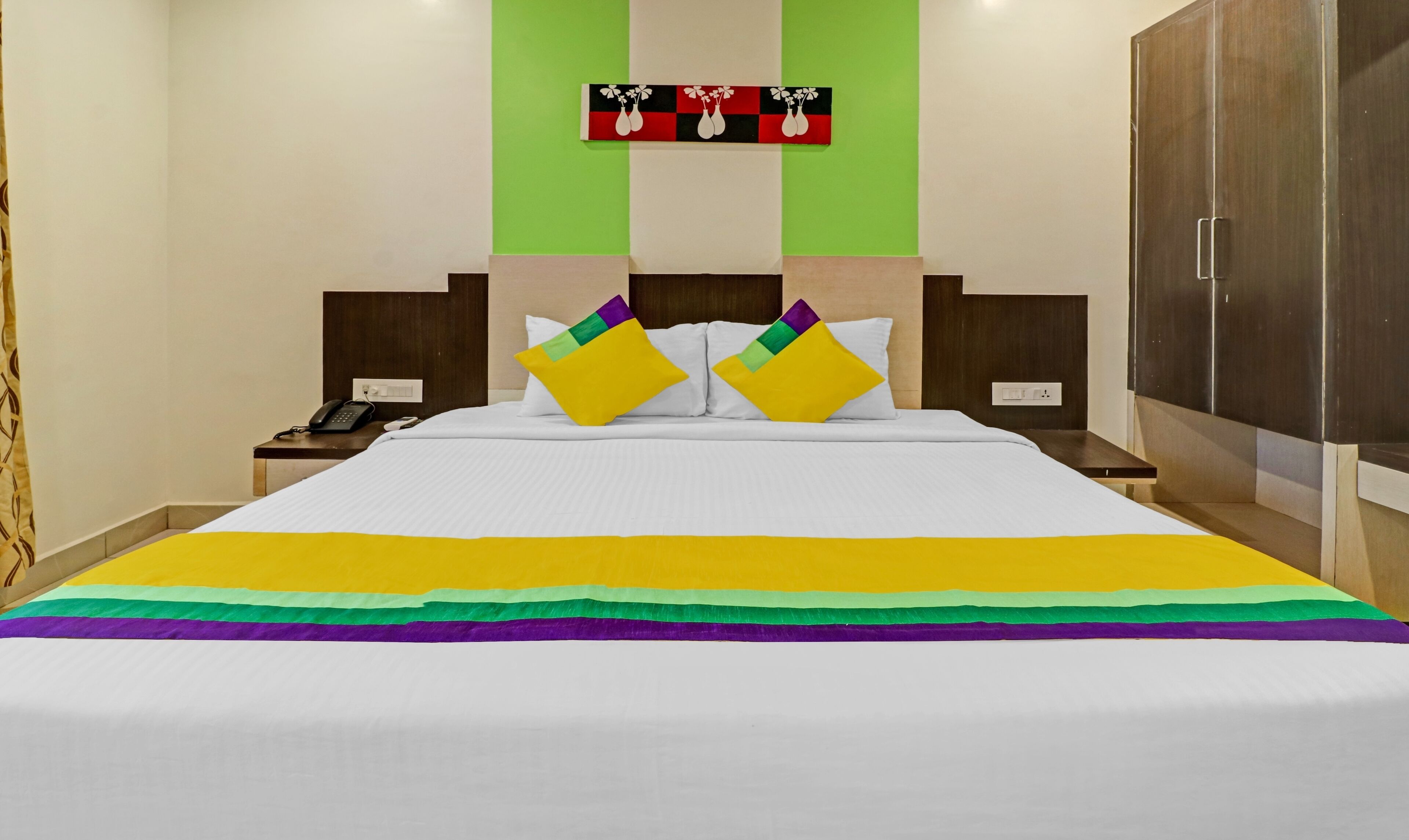 A hotel room with a large bed, two bedside tables, a phone, and a wall-mounted artwork.