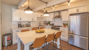 Una cocina moderna con armarios blancos, electrodomésticos de acero inoxidable y una isla de mármol con taburetes de bar.